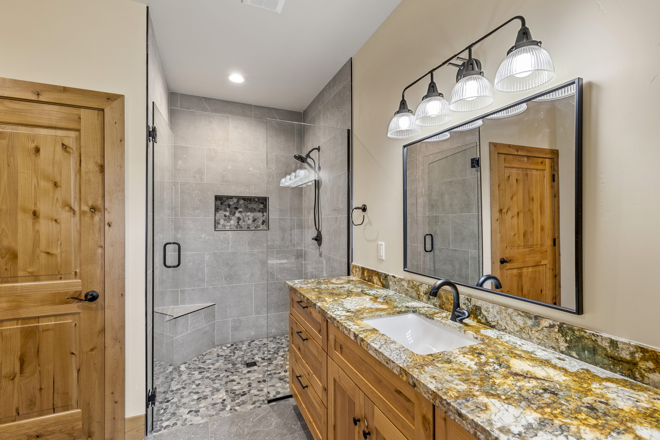 remodeled bathroom with large mirror, lots of counter space and a walk-in shower with a glass door